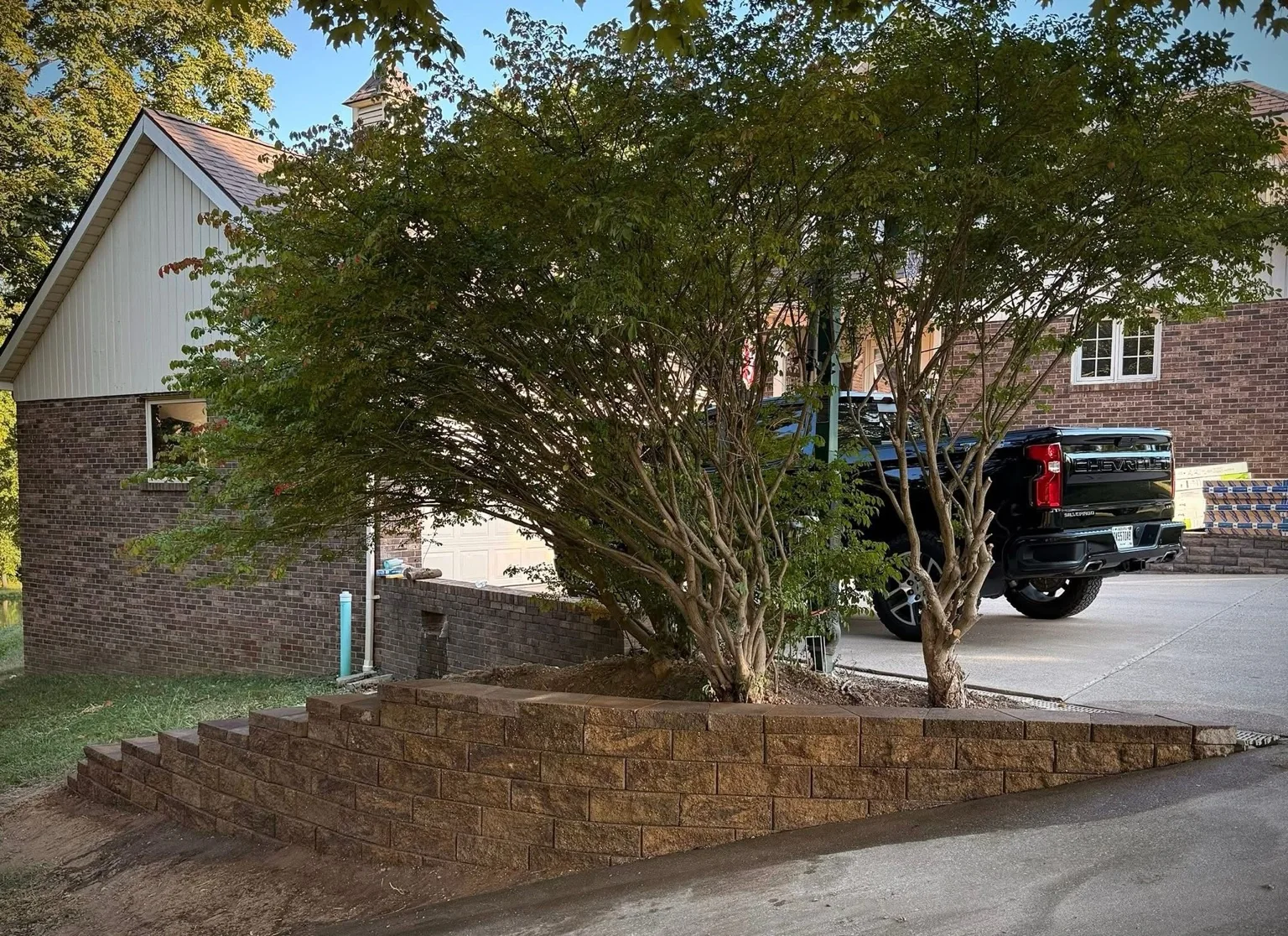 Tiered block retaining wall around mature trees beside a driveway