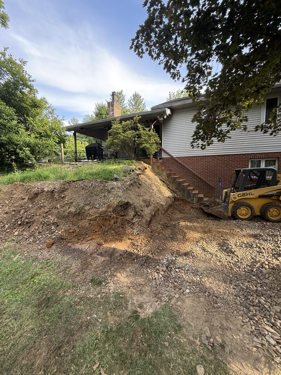 Skid steer and excavated hillside beside a home
