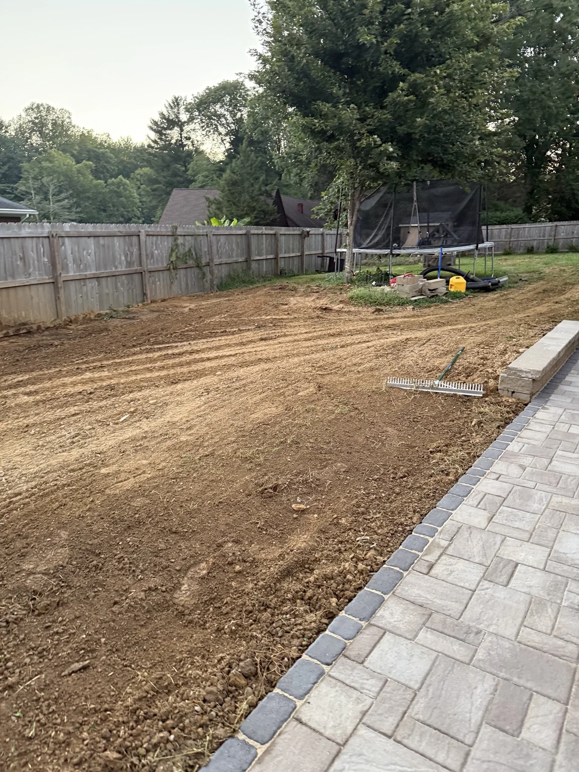 Backyard soil graded beside a completed paver patio