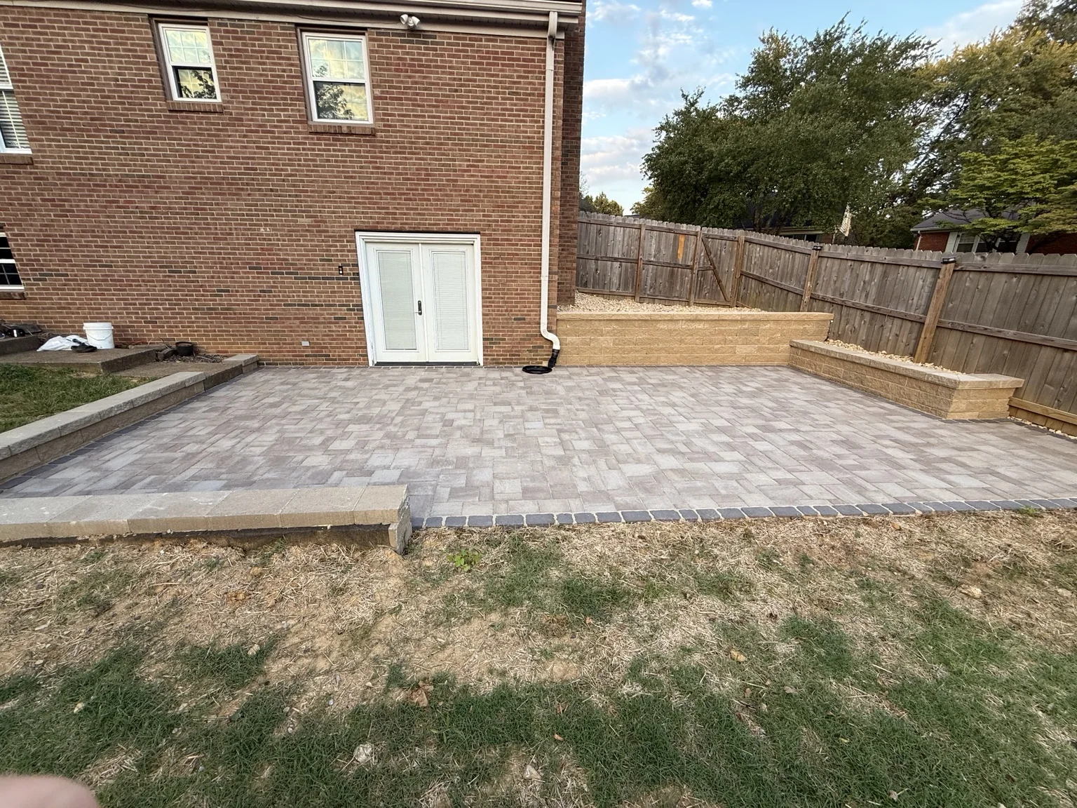 Completed paver patio with retaining walls beside a brick home